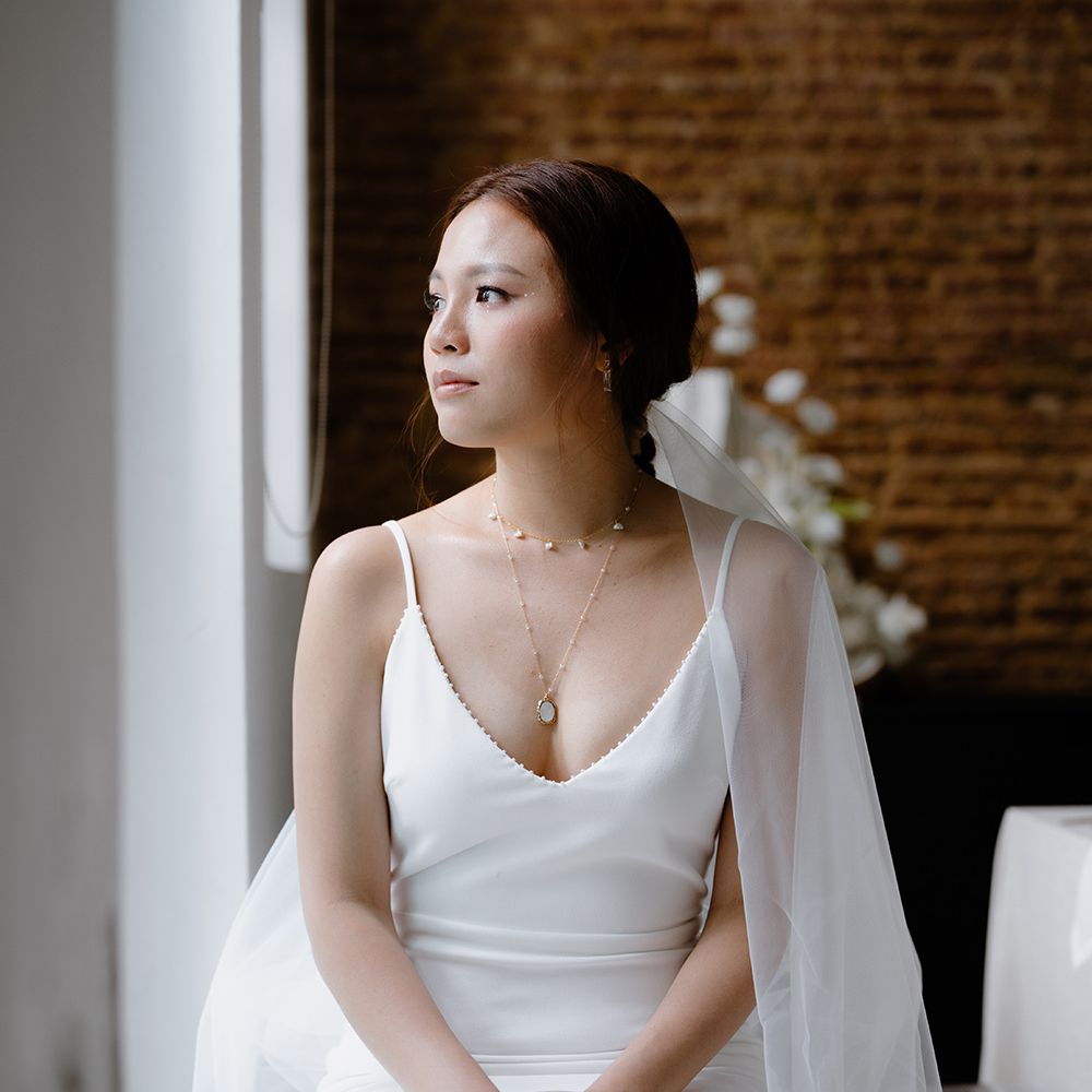 Asian bride in a minimalist wedding dress with gold necklaces and wedding veil 
