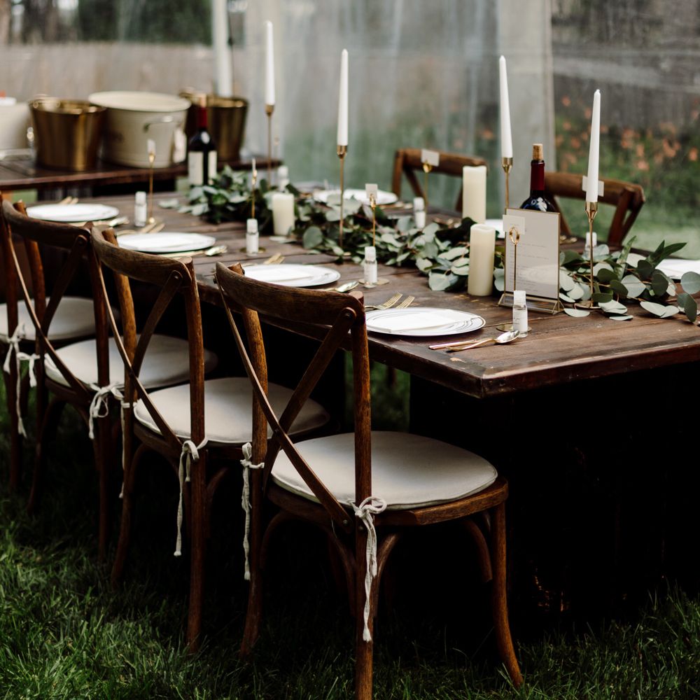 Dark wooden wedding breakfast table with wooden chairs, white candles and green leaf table garland for backyard wedding