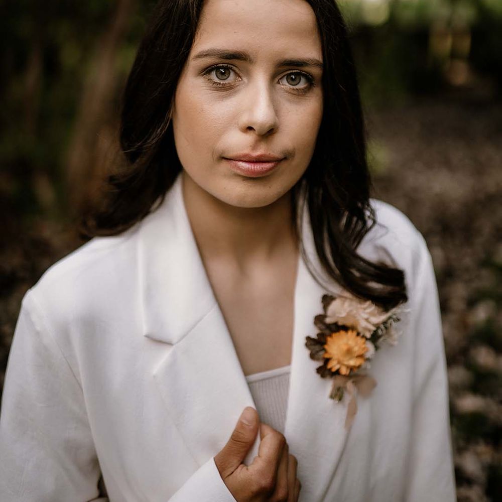 Beautiful bride with long hair in a white blazer and yellow buttonhole flower 