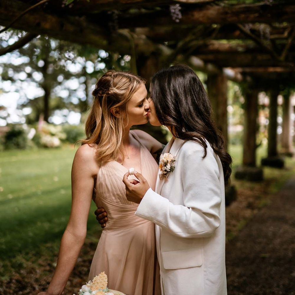 Brides kissing at their outdoor wedding reception under a pergola 