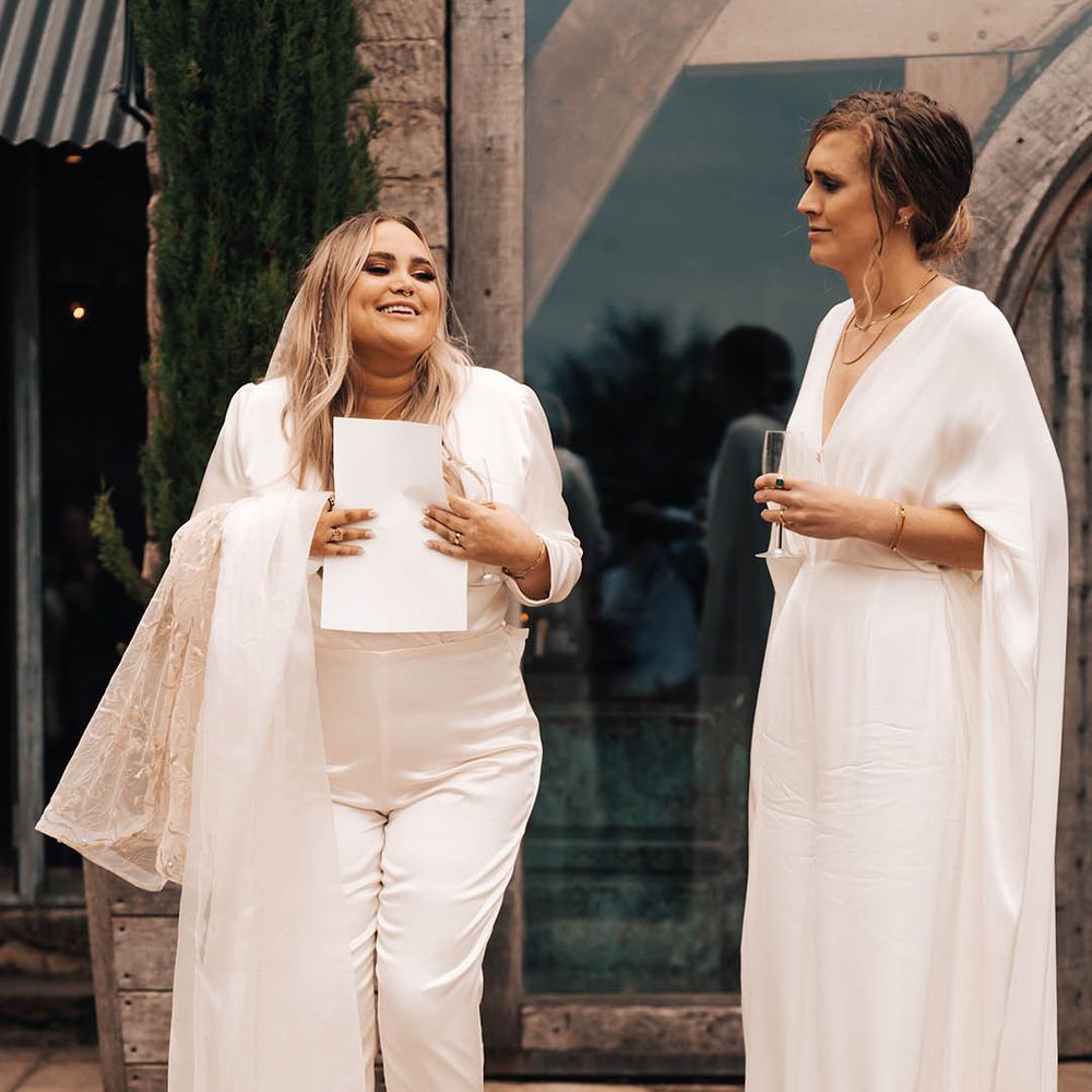 Brides stand together wearing white jumpsuits on their wedding day outdoors 