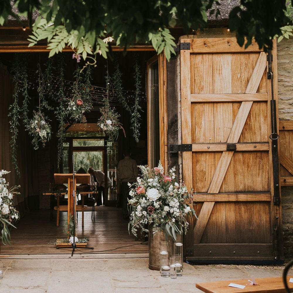 Barn doors at Tythe Barn with florals in milk churns, candle and hanging florals set up for wedding ceremony