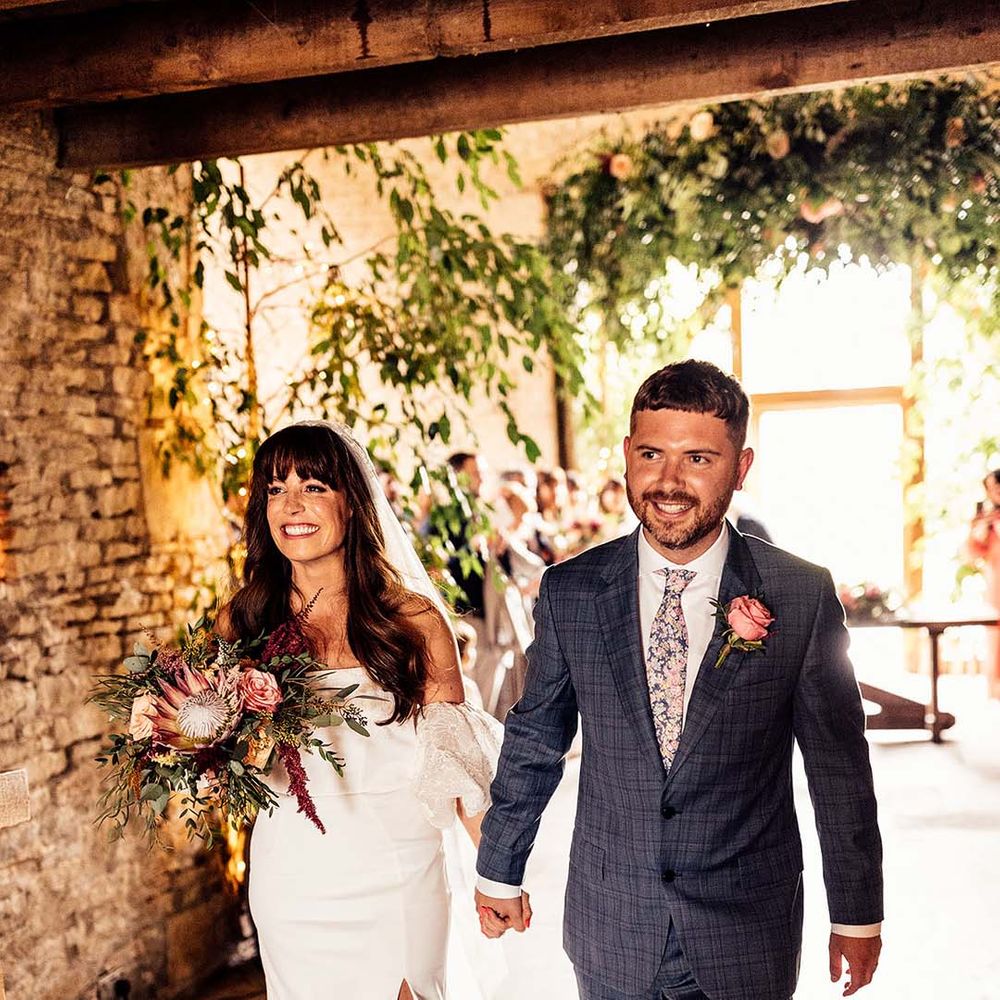 Bride & groom smile and hold hands as they walk with one another after their wedding ceremony