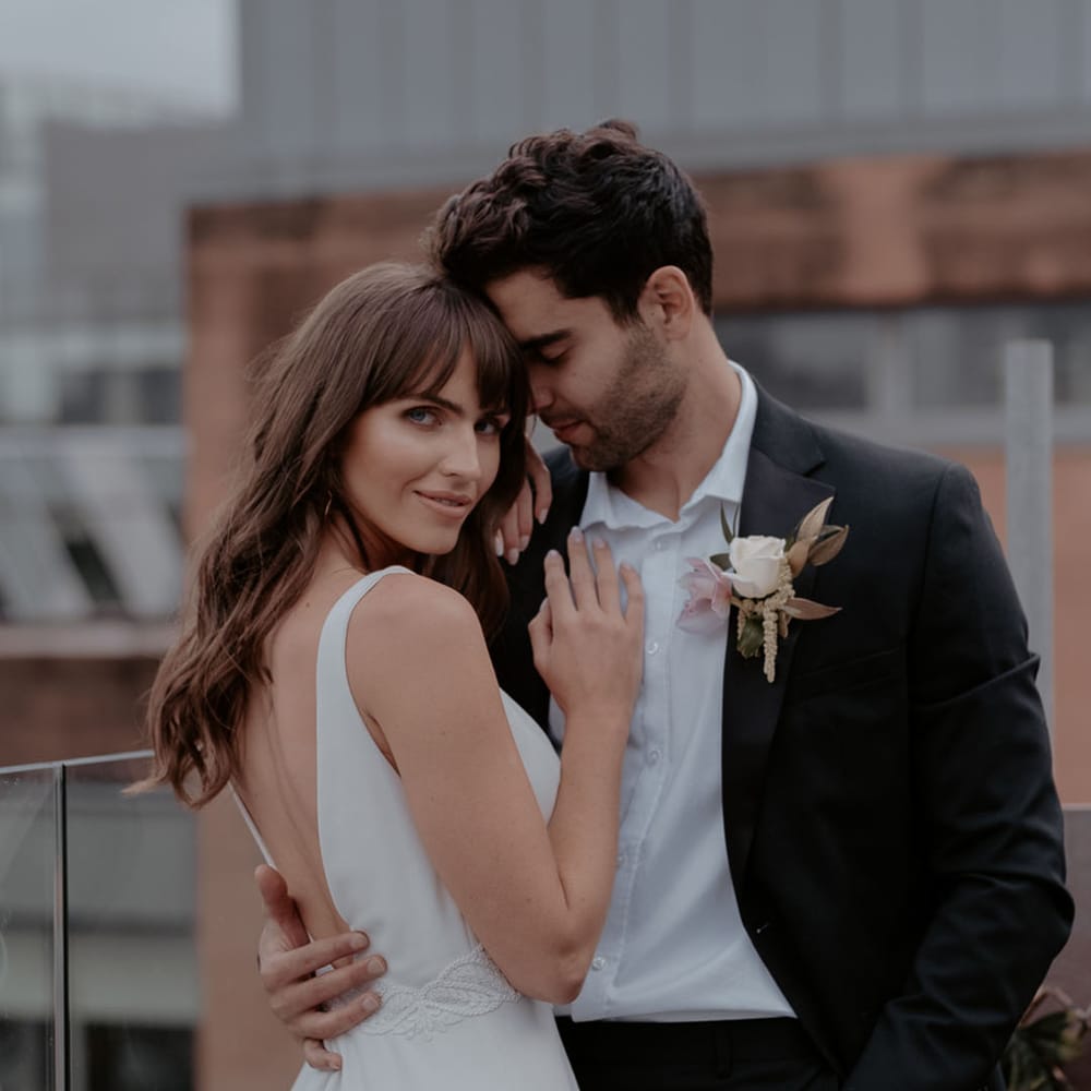 Bride with long wavy hair and a fringe embracing her husband in an A line wedding dress with love back