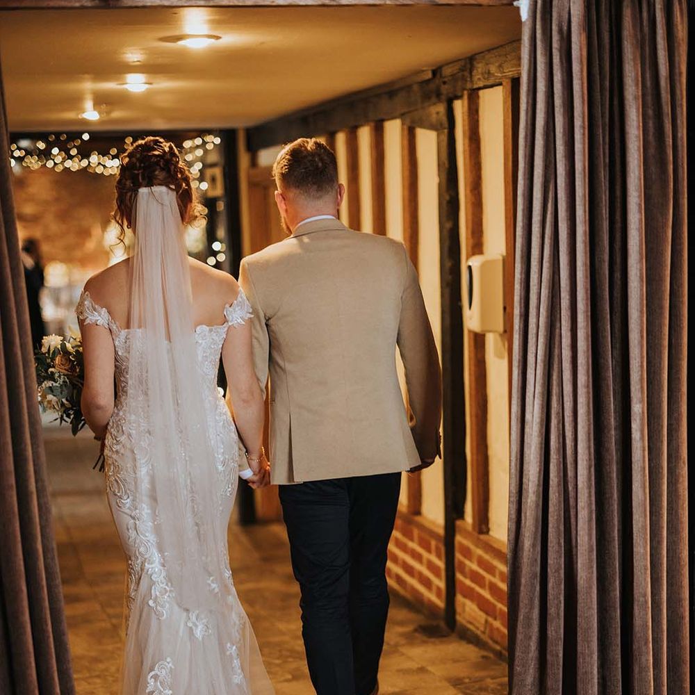 Bride with veil, lace off the shoulder wedding dress with train and groom in beige suit jacket