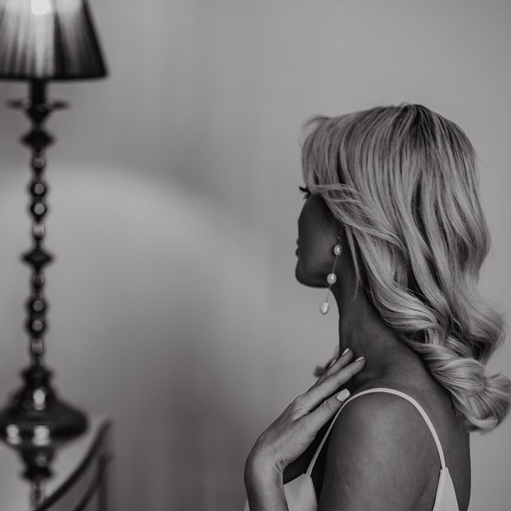 Bride with long wavy barrel curls and dangly pearl earrings on the wedding morning 
