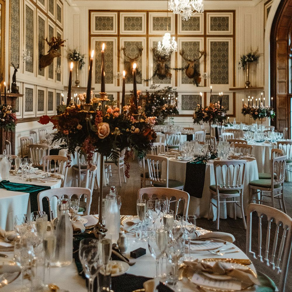 Table settings with black candles and rose wedding flower centrepieces with white napkins and plates and gold details 