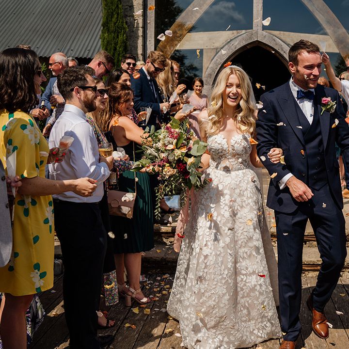 Groom in three piece blue suit with blue bow tie has confetti moment with bride in strapless lace Lillian West wedding dress