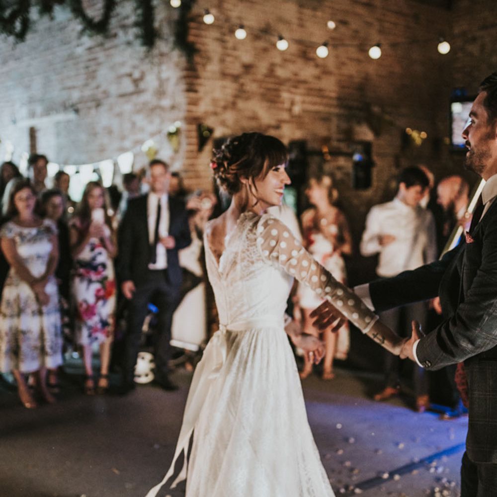 Bride in a long sleeve polka dot wedding dress being twirled on the dance floor at her rustic barn wedding 