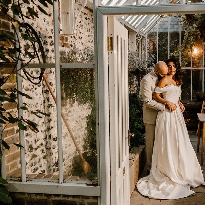 Groom embraces the bride from behind as they stand in the glasshouse at the Chapel House Estate 