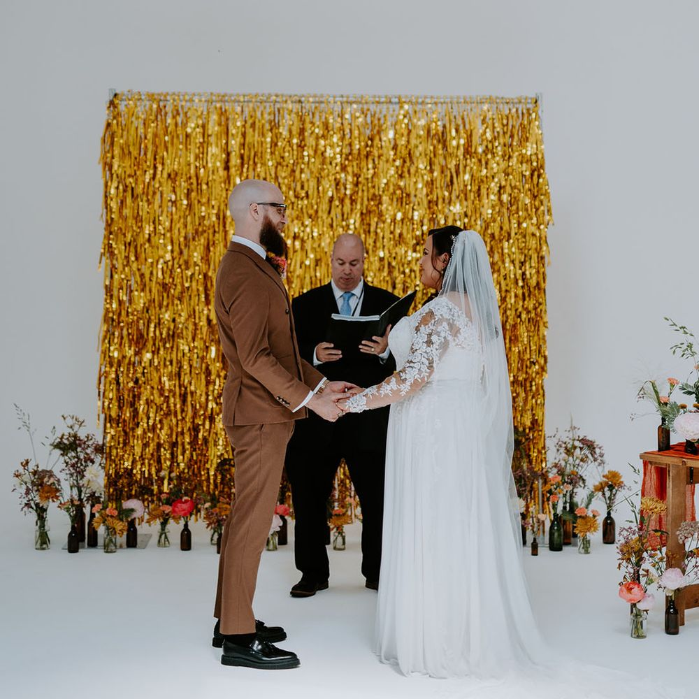 Bride & groom stand in front of gold streamers wedding decor during ceremony 