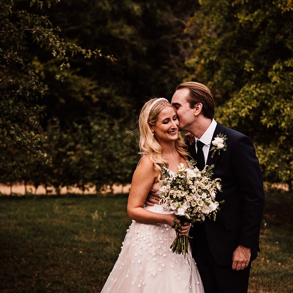 Groom in a navy blue suit kisses the bride in an applique wedding dress with flower design 