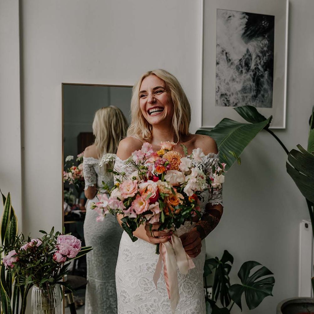 Bride in lace boho two piece smiling and laughing, holding colourful mixed floral bouquet 