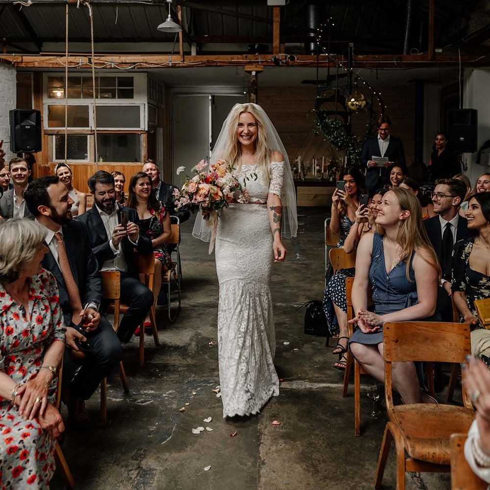Bride in lace boho two piece, colourful mixed floral bouquet and short veil walking down the aisle at Hackney Studios