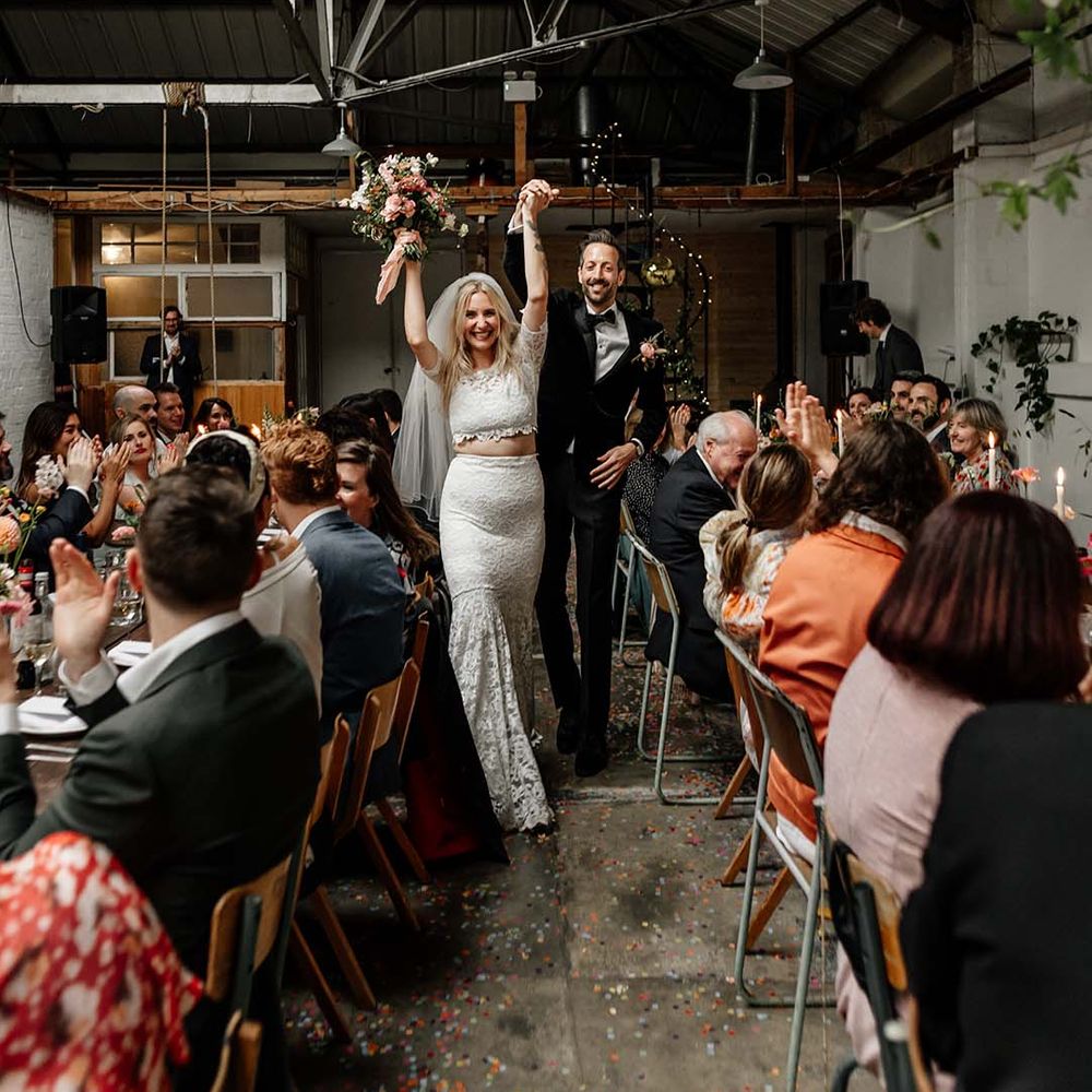 Bride in boho two piece lace bridal outfit and groom in black tux with velvet look bow tie cheering at wedding reception