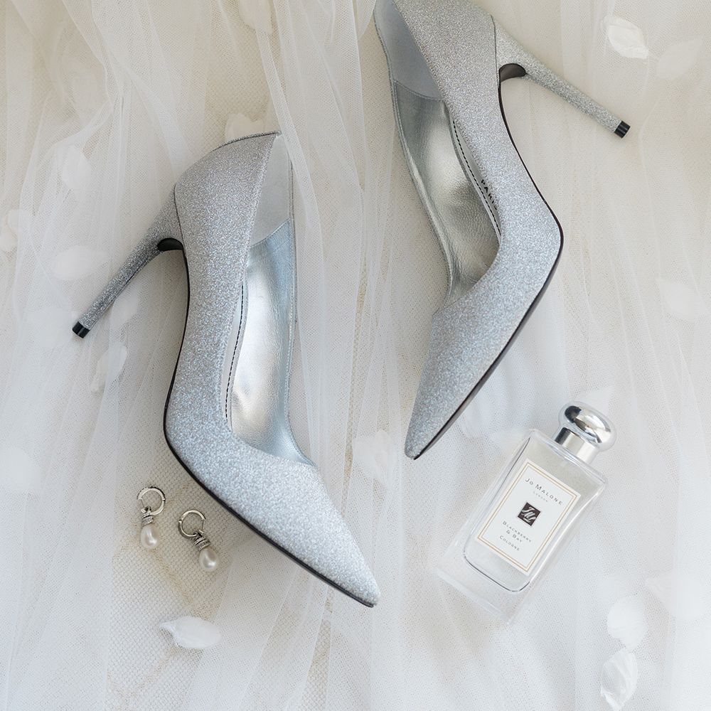 Silver glitter heeled bridal shoes beside pearl earrings and Jo Malone perfume 