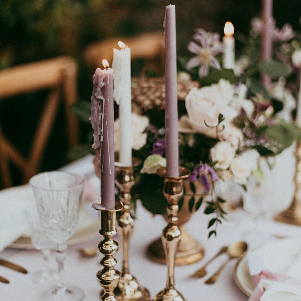 White and lavender tapered candles in gold candle holders on neutral wedding tablescape with gold accents