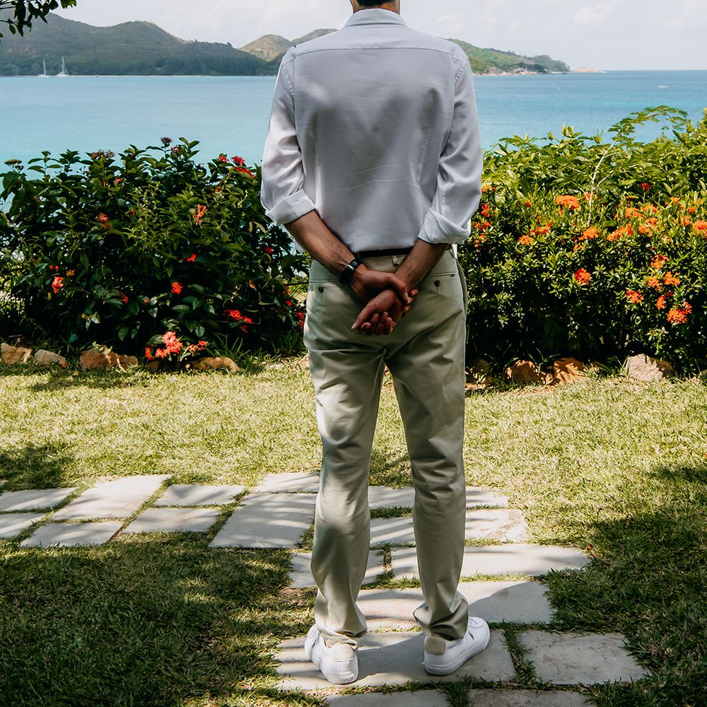 Groom in crisp white shirt, light coloured chinos, tan leather belt and white trainers waiting for bride at Seychelles elopement