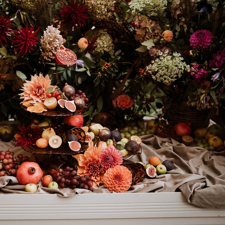 Wedding fruit tower on dark burgundy opaque cake stand surrounded by pink roses, baby's breath, eucalyptus, carnations, dahlia pinnatas and foliage