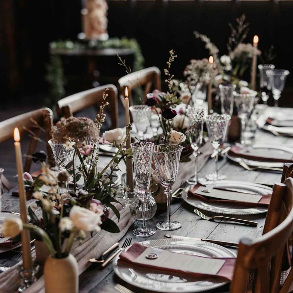 Rustic luxe wedding tablescape with white cloth table runners, foliage, baby's breath, eucalyptus and dried flower floral arrangements, neutral tapered candles and small ceramic vases 