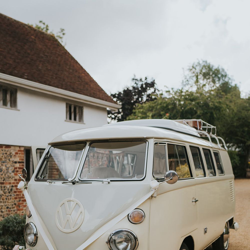 Cream VW wedding transport decorated with neutral wedding flowers and roses along the bumper of the car with white ribbon 