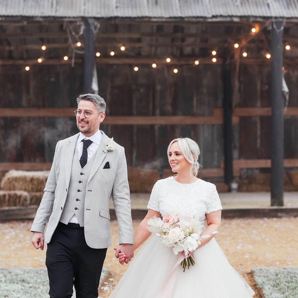 Bride in big princess tulle skirt with short sleeve top walking hand in hand with the groom in light grey suit jacket and waistcoat 