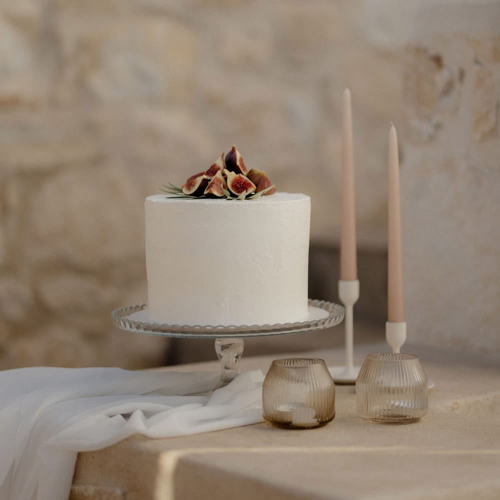 Simple iced wedding cake with figs and blush tapered candles at private villa wedding in Greece