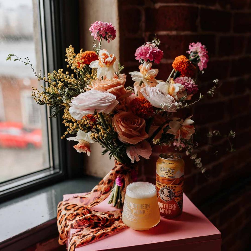 Colourful mixed flower bridal bouquet tied with leopard print ribbon on pink wedding stand with craft beer at Northern Monk Refectory Leeds