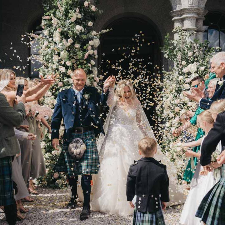Bride in mesh long sleeve wedding dress doing confetti exit with groom in wedding kilt and sporran at Cluny Castle wedding venue Scotland 