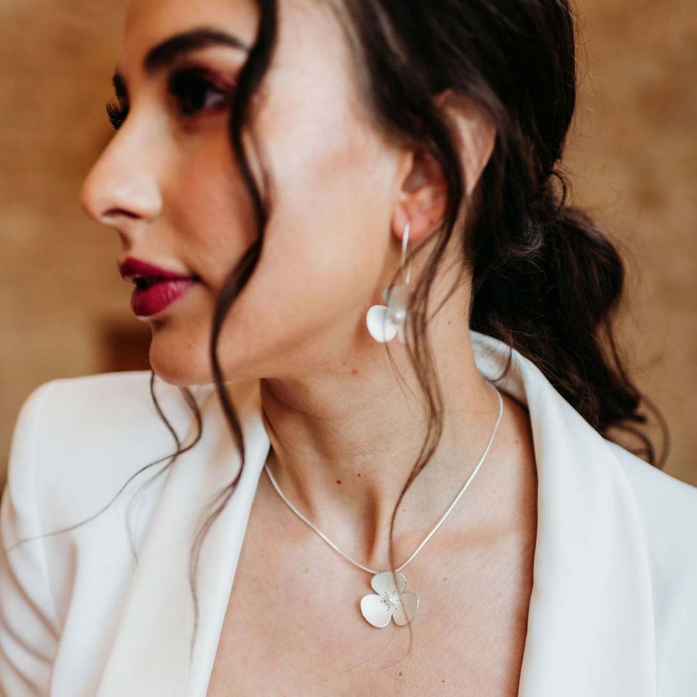 Bride in white bridal suit wearing dainty silver wedding jewellery with large flower designs at Merriscourt wedding