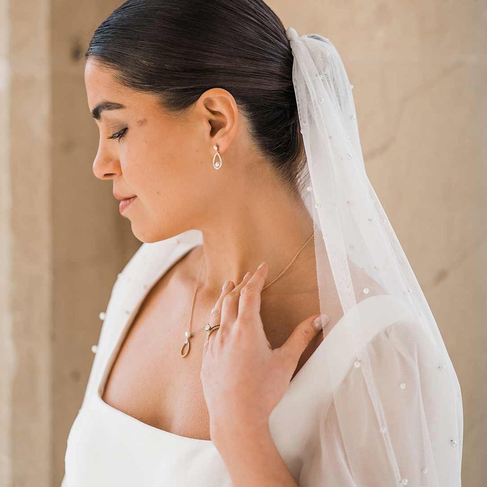 Bride in square neck wedding dress with sheer pearl embellished bridal veil and dainty silver pearl bridal jewellery 