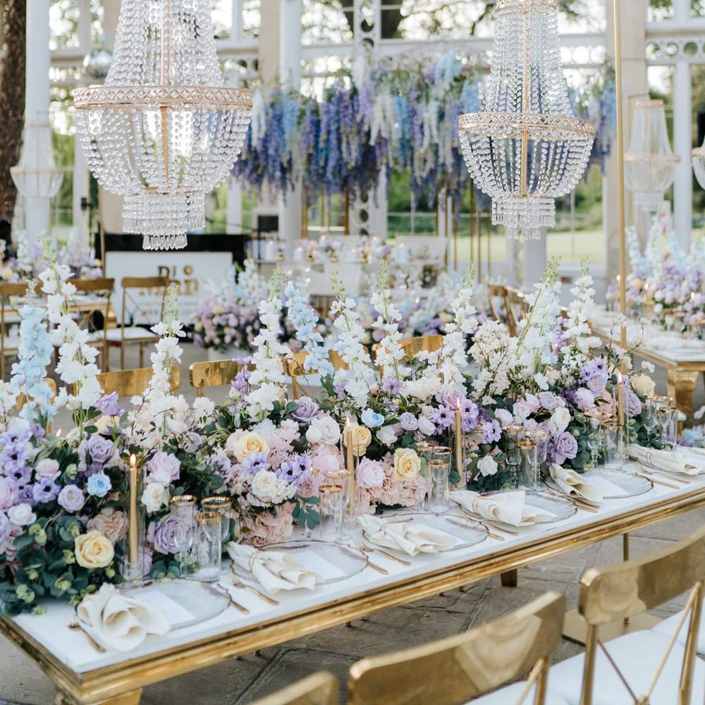 Syon Park wedding venue reception room with gold chairs, botanical tablescapes with large pastel flower centrepieces, gold tapered candles, gold rimmed tableware and suspended pastel foliage decor 