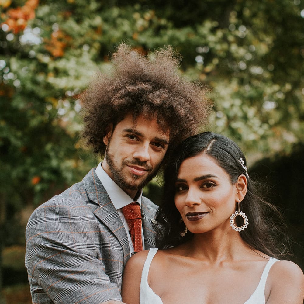Groom in grey and orange check suit embracing his bride 