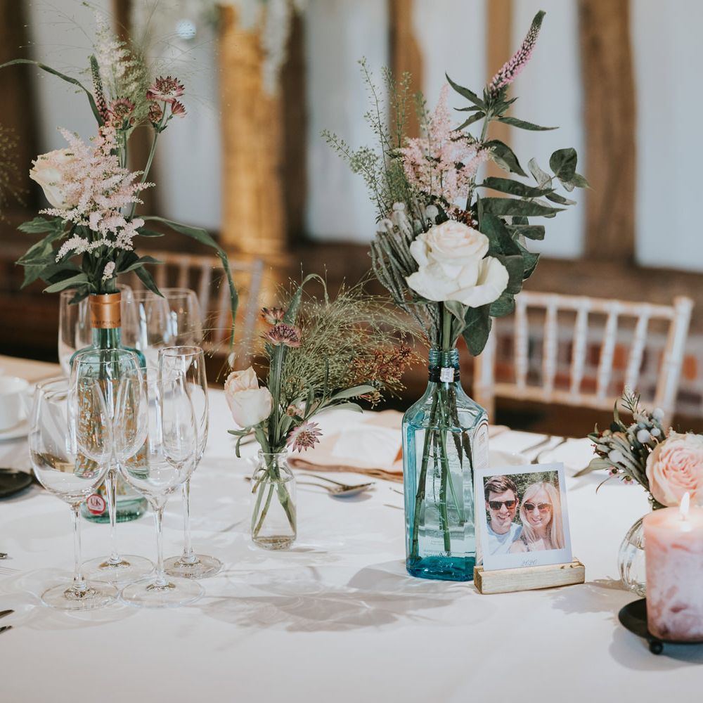 Table decor featuring personalised polaroids and florals in gin vases