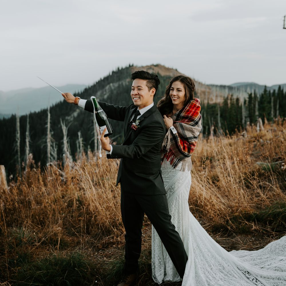 Groom sabres champagne with bride behind him