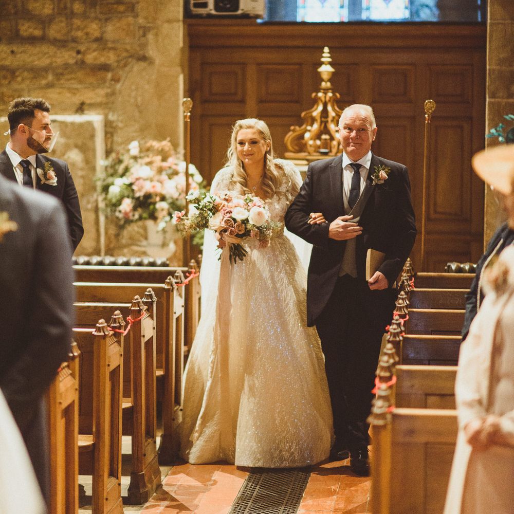 Father of the bride walking his daughter down the aisle at church wedding ceremony 