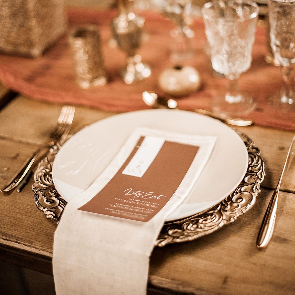 Place setting with gold charger place, gold cutlery and brown menu card 