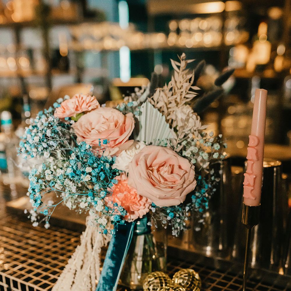 Pink rose and blue gypsophila wedding bouquet tied with teal velvet ribbon resting on the bar 