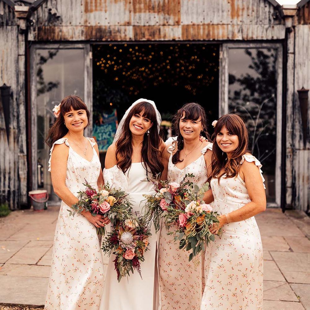 Bride stands with her bridesmaids who hold colourful floral bouquets as floral gowns
