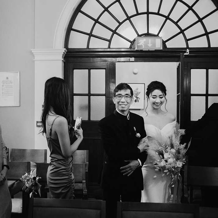 Father of the bride in dark suit walks bride down the aisle 