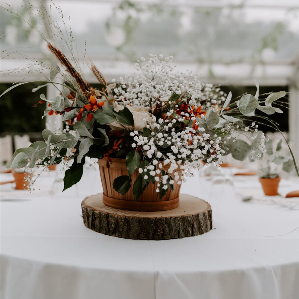 Wooden pot full of mixed white, red and green foliage on table at marquee wedding reception in Bedfordshire