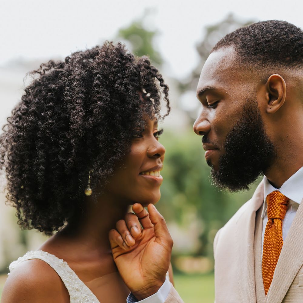 Intimate wedding portrait of groom holding his bride's chin with naturally curly hair and plunging neckline wedding dress
