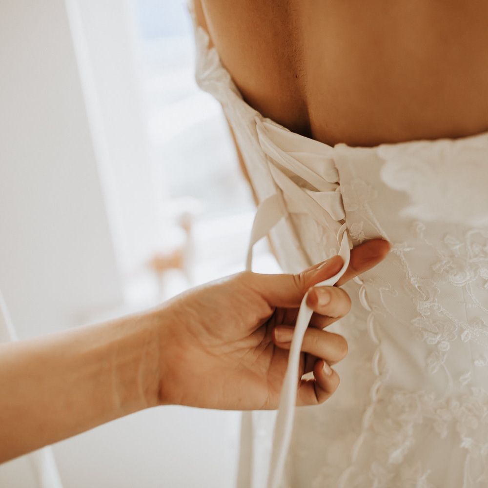 Bridesmaid does up the ribbons on bride's lace corset back wedding dress