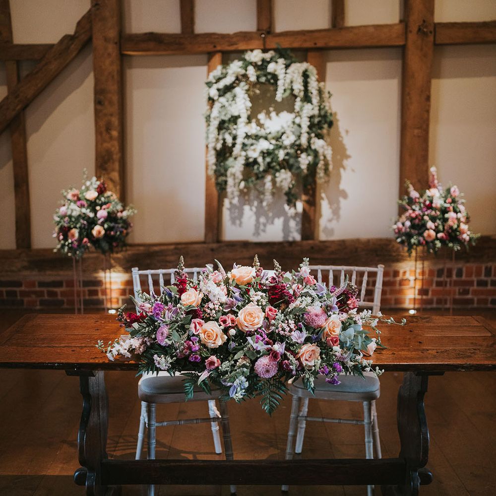 Dark wooden table with large flower displays of pink, white, orange and purple flowers at rustic country house venue