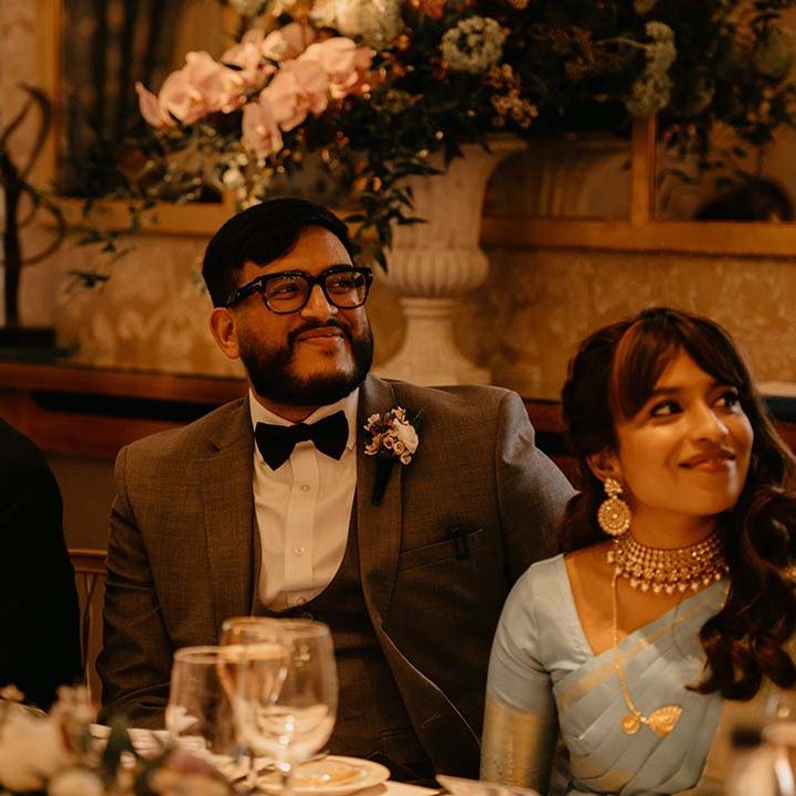 Bride in mint green saree with groom in grey suit with black bow tie and neutral boutonniere 