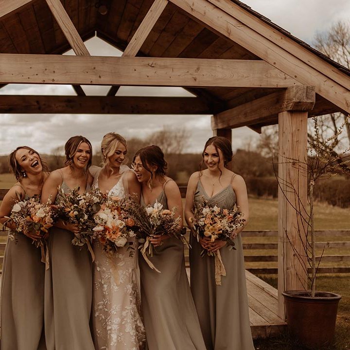 Bride laughs and smiles with her bridesmaids in green dresses outside Eden Barn wedding venue after the rustic barn wedding 