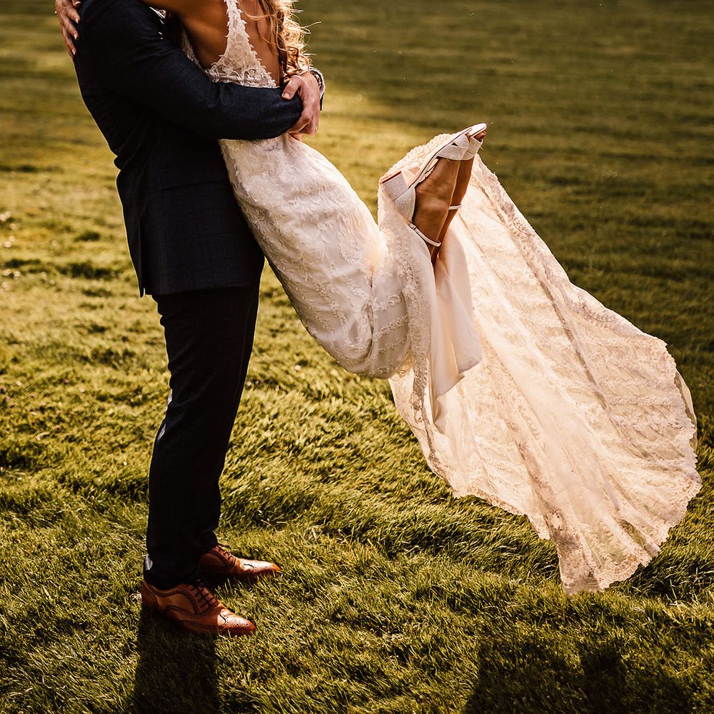 Groom in blue suit lifts the bride in a kiss with the bride wearing sparkly Charlotte Mills wedding shoes 