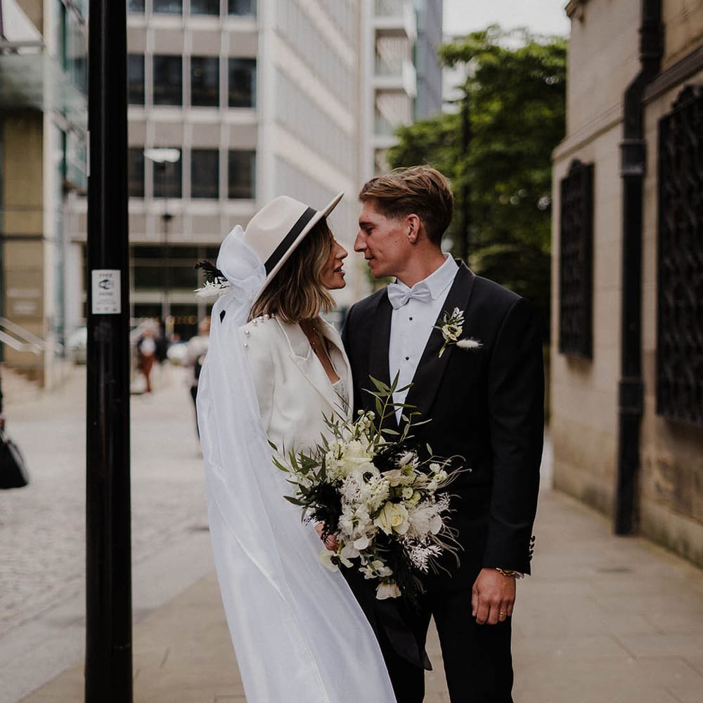 Bride in white trouser Nadine Merabi pearl suit with groom in black tie and pale blue bow tie for town hall wedding 