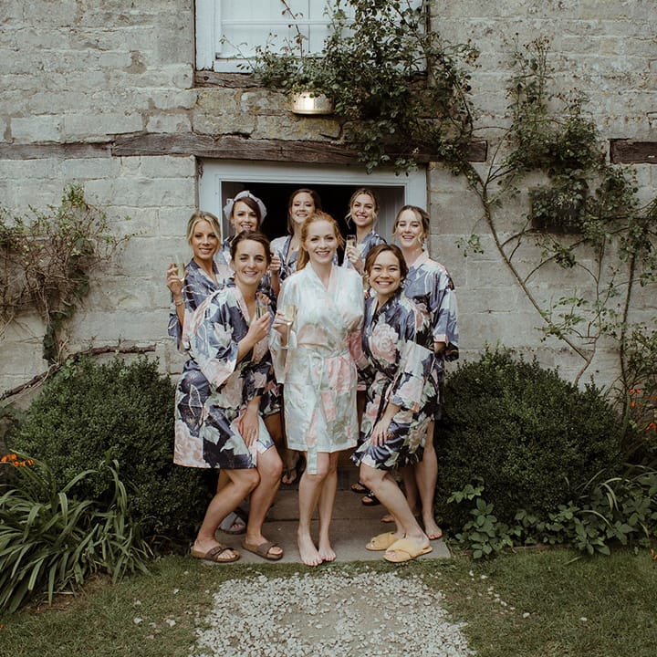 Bride in pastel pink and green floral satin robe with bridesmaids in darker blue floral satin robes for Owlpen Manor wedding 