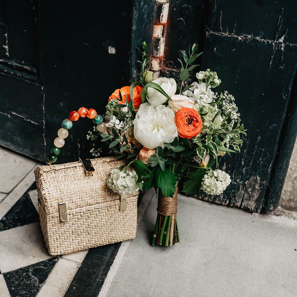 White & orange floral bridal bouquet next to wicker purse complete with brightly beaded handle 